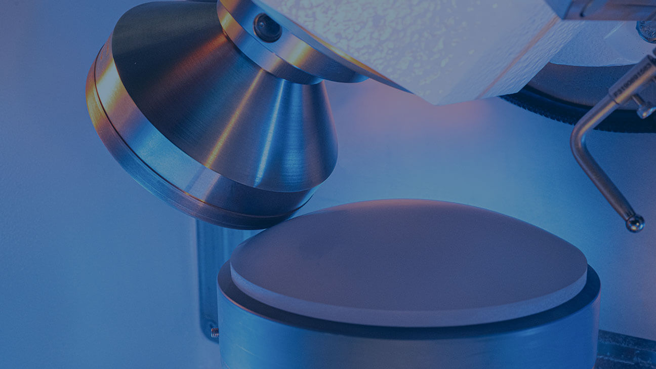 Close-up of laboratory equipment with a conical tool positioned above a flat cylindrical sample