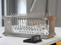 Stainless steel laboratory rack holding multiple pipettes or sample holders, placed on a table.