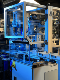 Automated laboratory robot system with mechanical arms handling sample vials under blue lighting.